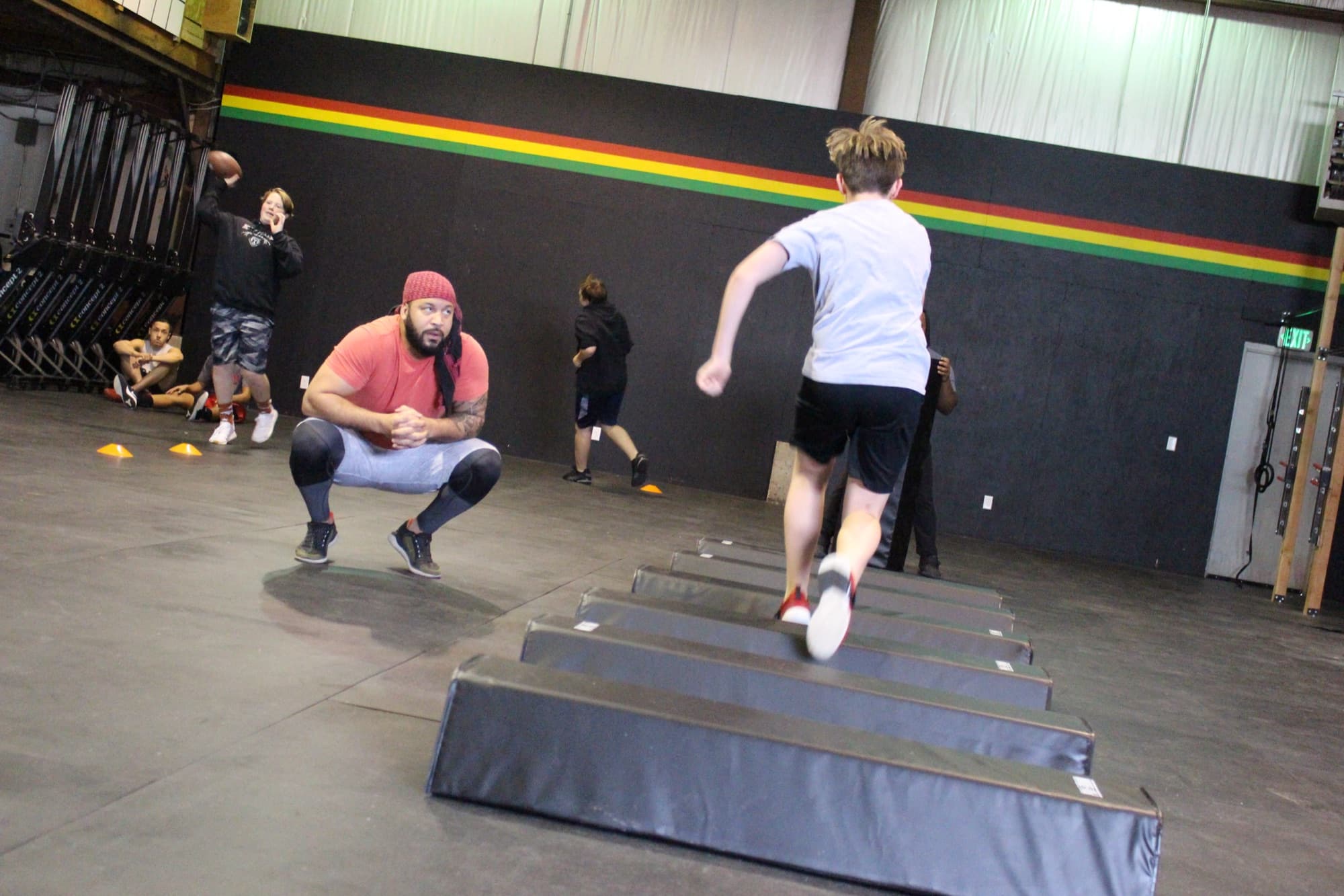 Coach Matt Byrd in a red shirt and beanie coaching a kid through plyo jumps